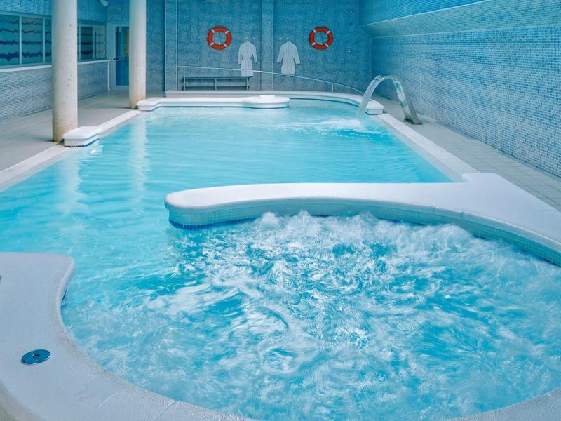 Piscina interna con vasca idromassaggio adiacente in un'area benessere con piastrelle blu.