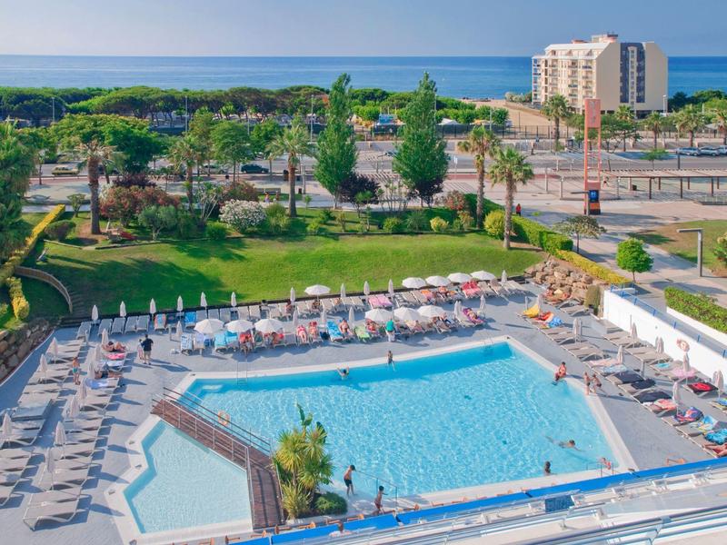 Piscina dell'hotel con lettini, vista sul mare e sugli edifici circostanti con tempo soleggiato.