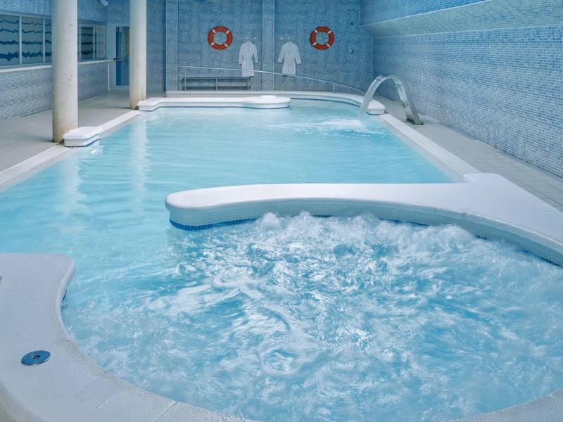 Piscina interna con area vasca idromassaggio e pareti piastrellate blu.