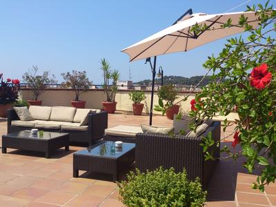 Rooftop terrace with rattan furniture, plants, and umbrella under clear sky.