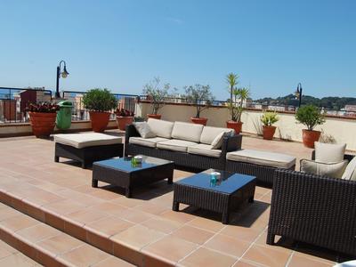 Terraza en la azotea con muebles, mesas y macetas con plantas bajo cielo despejado.