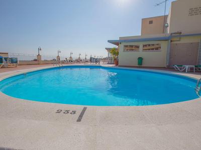 Una piscina ovalada con agua azul clara en una terraza de hotel bajo un cielo soleado.