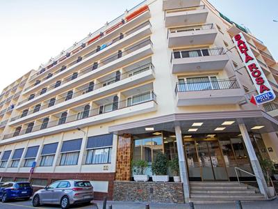 Edificio de hotel de varios pisos con balcones y autos en el estacionamiento frente a él.