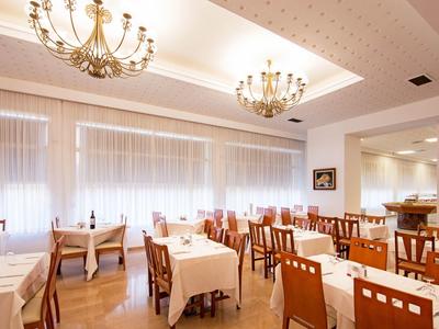 Restaurante luminoso con mesas de madera y manteles blancos, candelabros decorativos y grandes ventanas.