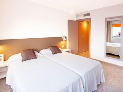 Habitación de hotel luminosa con dos camas individuales, mesitas de noche y espejo en la pared.