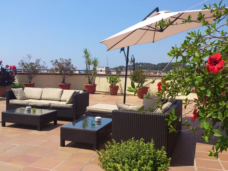 Terraza moderna con muebles de mimbre, sombrilla y flores bajo cielo despejado.
