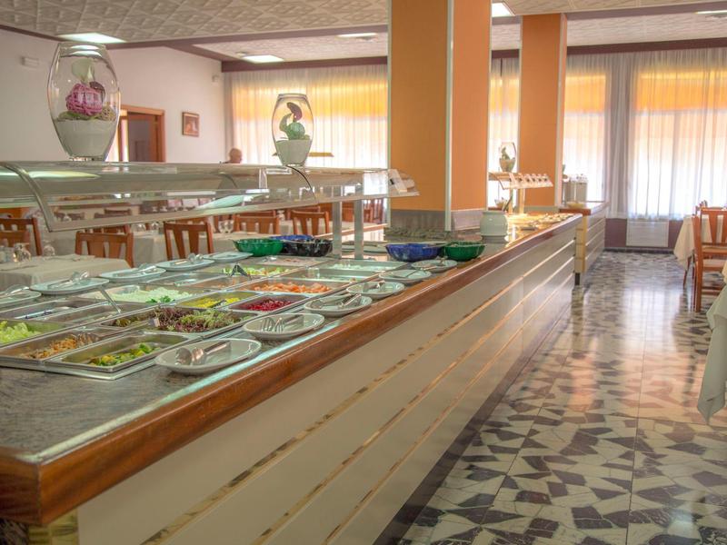 Restaurante luminoso con buffet, mesas y sillas, grandes ventanas y suelo de mosaico.