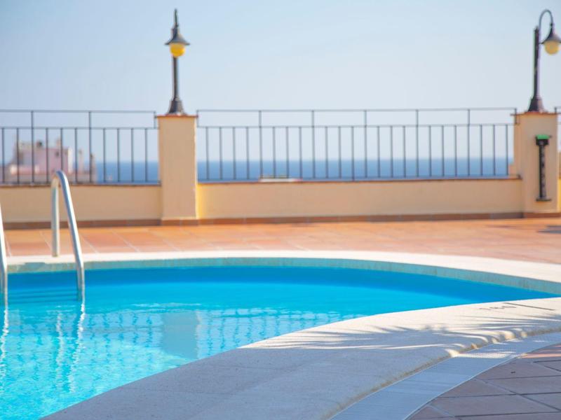 Piscina exterior climatizada con escalera y farolas en una terraza bajo cielo despejado.