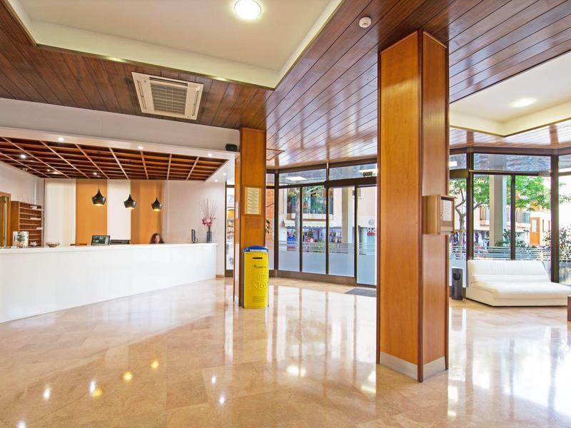 Lobby de hotel luminosa con suelo de mármol, elementos modernos de madera y gran recepción.