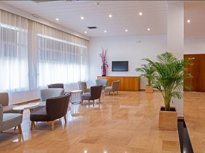 Amplia y luminosa sala de estar de hotel con sillones, sofás y grandes ventanas.