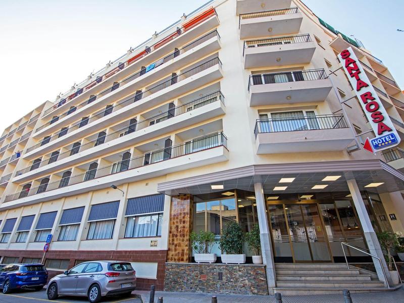 Edificio de hotel de varios pisos con balcones y autos en el estacionamiento frente a él.