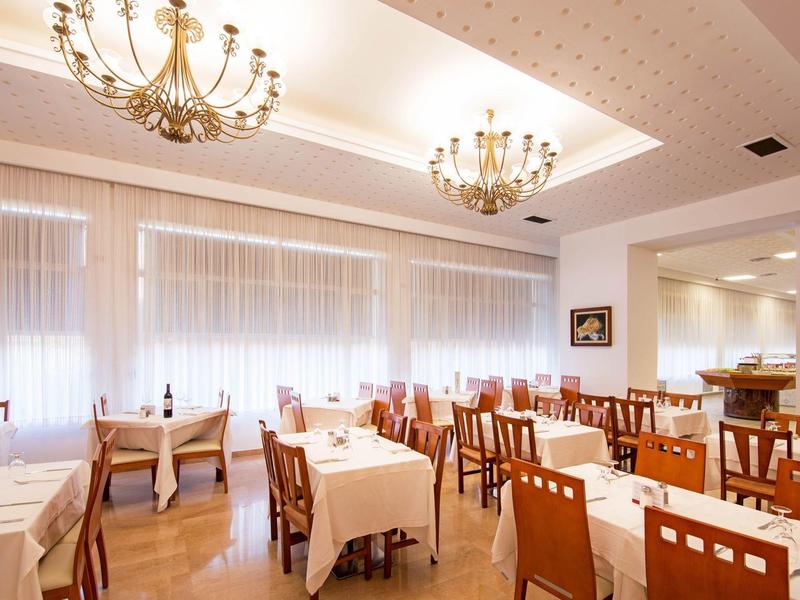 Restaurante luminoso con mesas de madera y manteles blancos, candelabros decorativos y grandes ventanas.