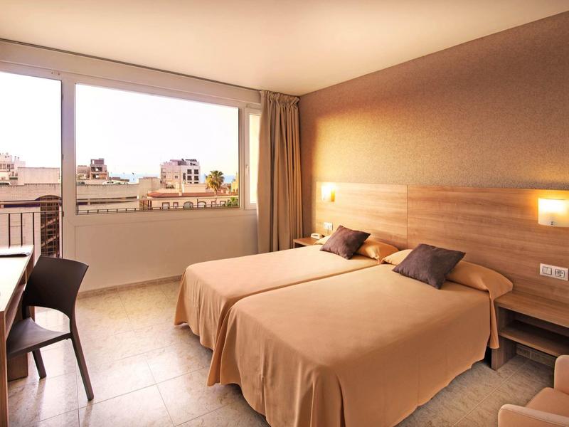 Habitación doble luminosa con dos camas, escritorio y vista a la ciudad por ventana grande.