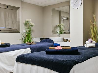 Moderne spa-kamer met twee bedden, zwarte handdoeken en planten voor ontspanning.