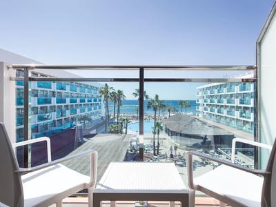 Uitzicht vanaf balkon met stoelen op hotelcomplex en zee onder heldere lucht.