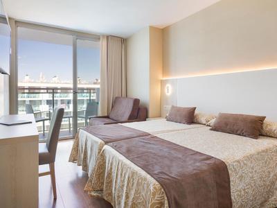 Lichte hotelkamer met tweepersoonsbed, stoel, bureau en balkon met uitzicht op zee.