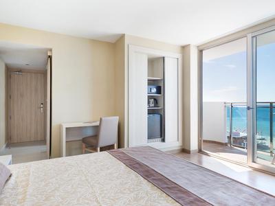 Helles Hotelzimmer mit Bett, Schreibtisch und Balkon mit Meerblick.