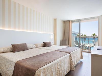 Lichte hotelkamer met twee bedden, balkon en zeezicht.