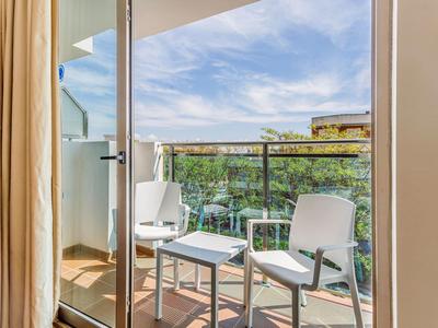 Balkon met twee witte stoelen en een kleine tafel, uitzicht op groen landschap en blauwe lucht.
