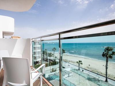 Balkon met witte stoelen en glazen balustrade met uitzicht op strand en zee.