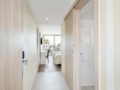 Gang met houten bekleding leidt naar een hotelkamer met tweepersoonsbed en raam met zeezicht.