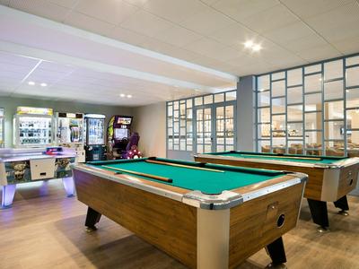 Moderne speelruimte met biljarttafels, airhockey en speelautomaten in een lichte kamer.