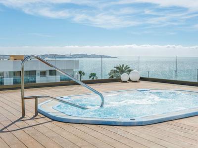 Whirlpool op houten terras met zeezicht en glazen afscheiding bij heldere hemel.