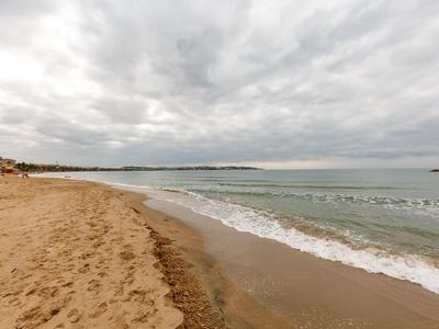 Strand met nat zand en rustig water onder een bewolkte hemel.