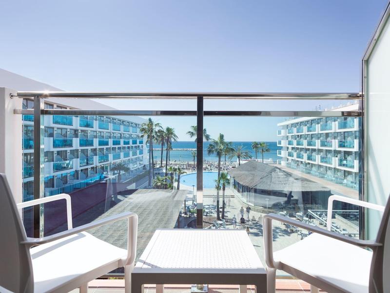 Uitzicht vanaf balkon met stoelen op hotelcomplex en zee onder heldere lucht.