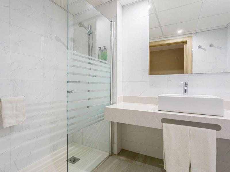 Lichte badkamer met inloopglazen douche, wasbak op lang aanrecht en grote spiegel.