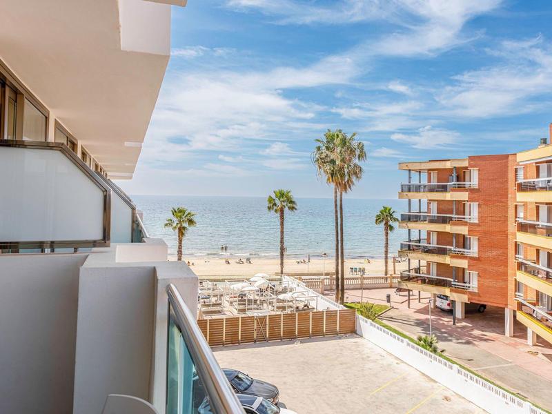 Uitzicht vanaf een hotelbalkon op zee, zandstrand en palmbomen onder een blauwe lucht.
