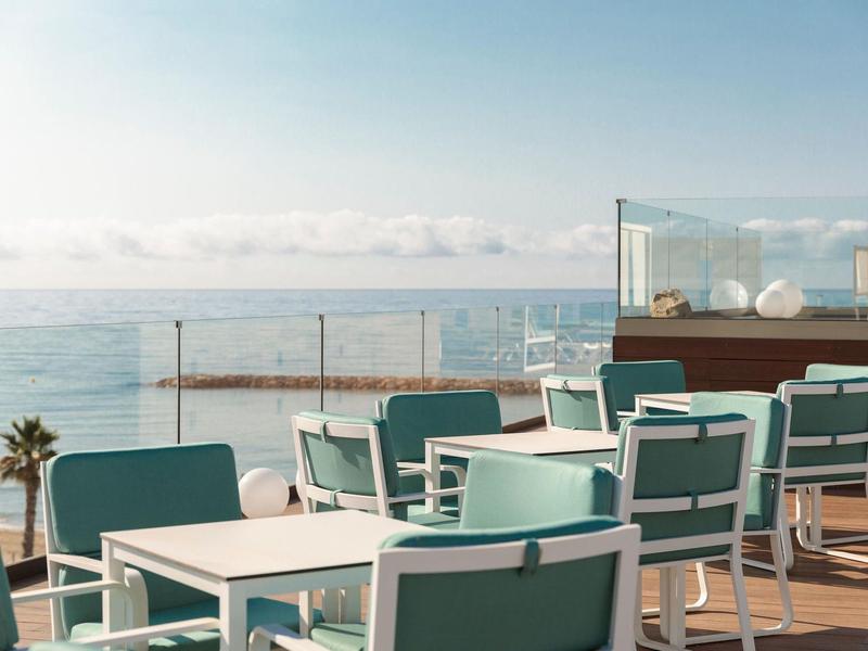 Terras met stoelen en tafels met uitzicht op zee onder een bewolkte lucht.