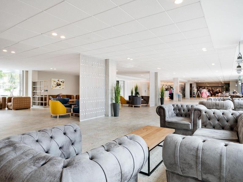 Ruime moderne hotel lobby met grijze zitmeubels en lichte vloer.