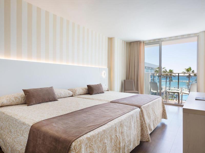 Lichte hotelkamer met twee bedden, balkon en zeezicht.