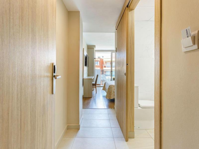 Gang met lichte muren, uitzicht op woonruimte en balkon aan het einde.