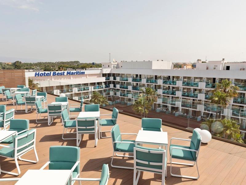 Dakterras met witte tafels en turquoise stoelen, hotelgebouw op de achtergrond.