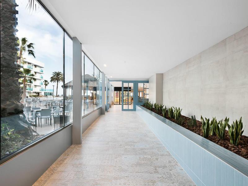 Lichte gang met glazen ramen en planten, moderne terras met zitplaatsen zichtbaar.