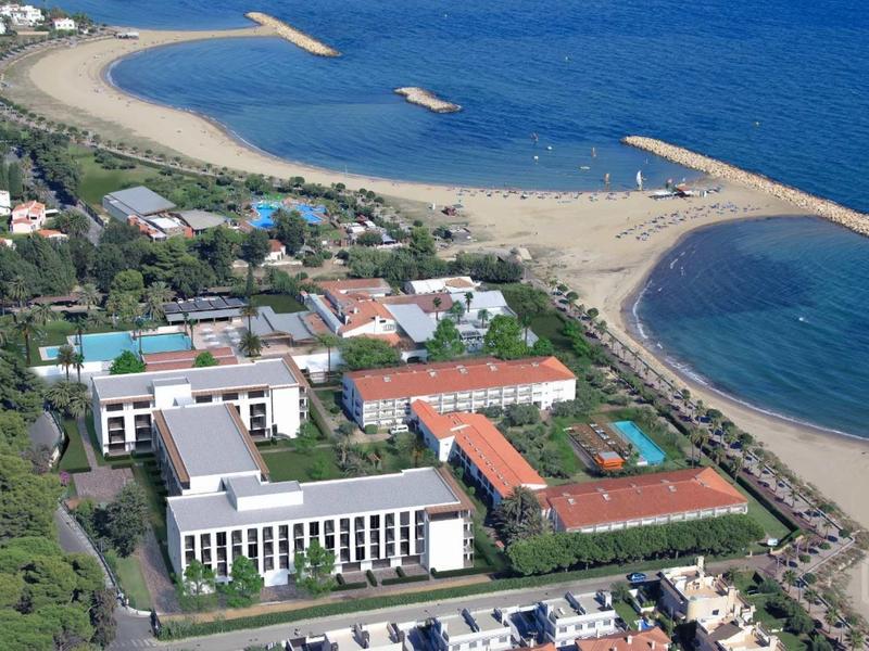 Aerial view of a hotel by the beach and blue sea with tennis courts.
