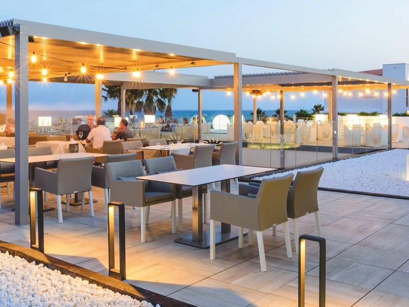 Modern hotel outdoor terrace with illuminated pergolas and seating areas at dusk.