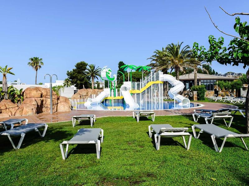 Water park with water slides and lounge chairs on green grass under blue sky.