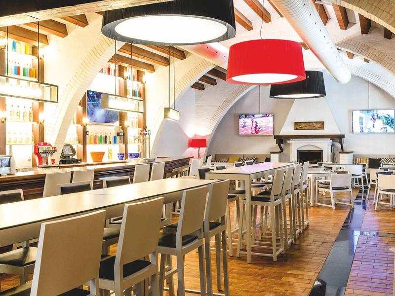 Interior of a modern hotel bar with high tables, chairs, and decorative lighting.