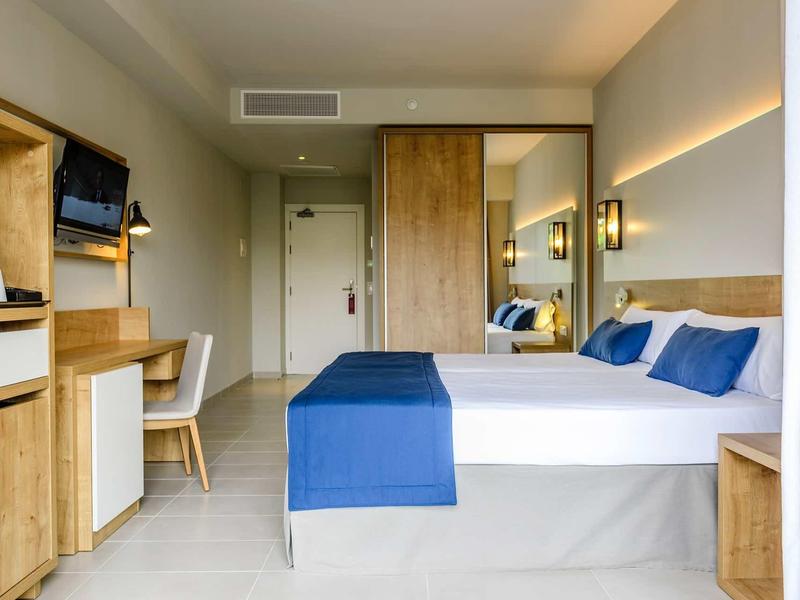 Modern hotel room with double bed, wooden furniture, and blue-white bedding.