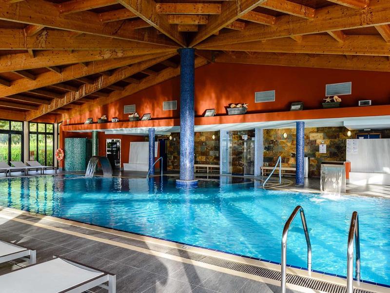 Indoor pool with wooden ceiling, large windows, and lounge chairs in a hotel