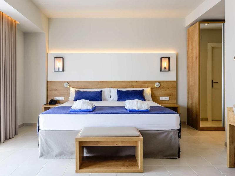 Modern hotel room with large bed, wooden furniture, and neutral tones.