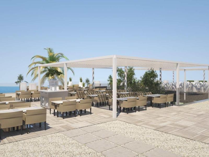 Open terrace area with tables and chairs, sea view, and blue sky in the background.
