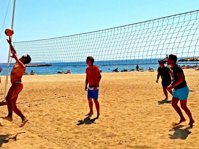 People playing volleyball on sunny beach with blue sky and sea in the background