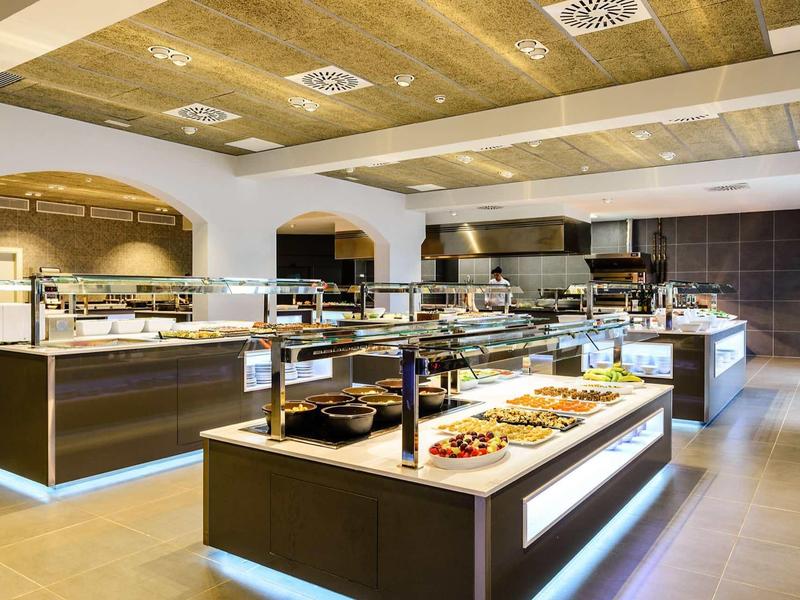 Modern hotel buffet with various dishes on illuminated counters in bright, spacious room.