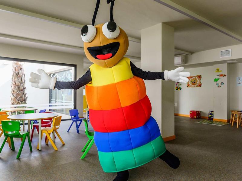 Colorful, friendly butterfly costume indoors with children's tables and chairs.