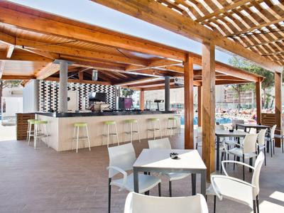 Área exterior moderna de un bar de hotel con asientos y techo de pérgola a plena luz del día.