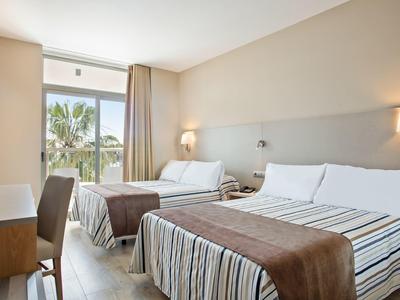 Habitación de hotel luminosa con dos camas y ventana con vista a palmeras.